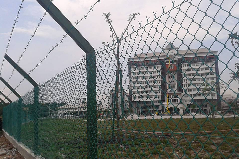 Chain link fence with barbed wire topping is placed along the industrial building.