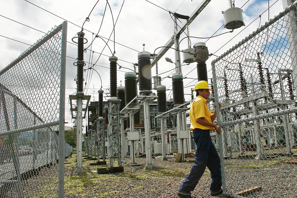 A maintenance worker opens the chain link fence gate for power facility inspection.