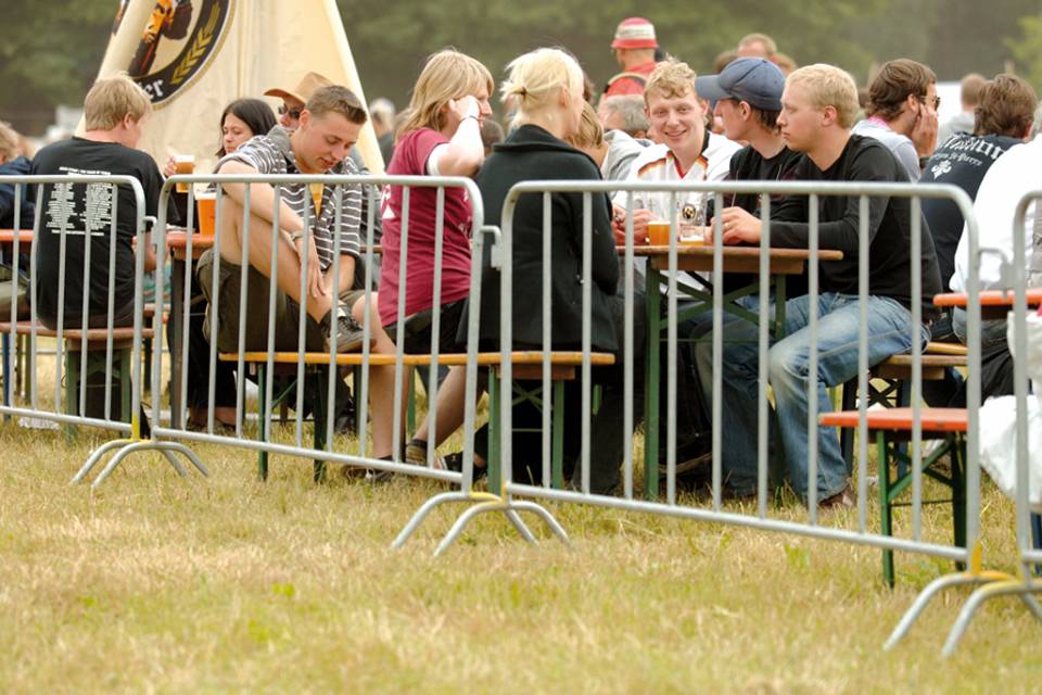 Many people are sitting and having drinks in the open air restaurant encircled by crowd control barrier.