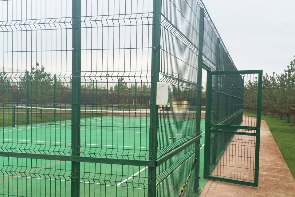 A sports field is enclosed by curvy welded fence.