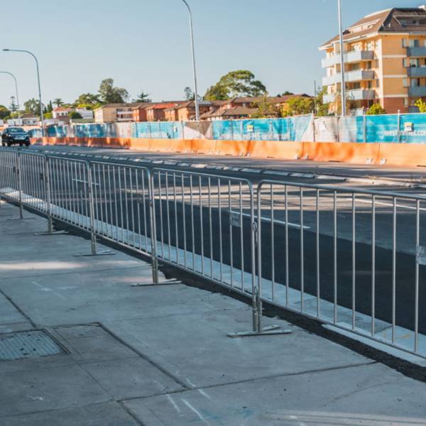 Galvanized crowd control barriers are installed along the road.